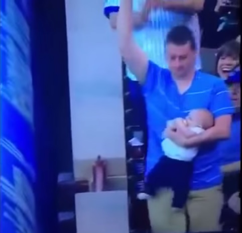 Papà multitasking: afferra palla con la mano, in braccio ha figlio neonato